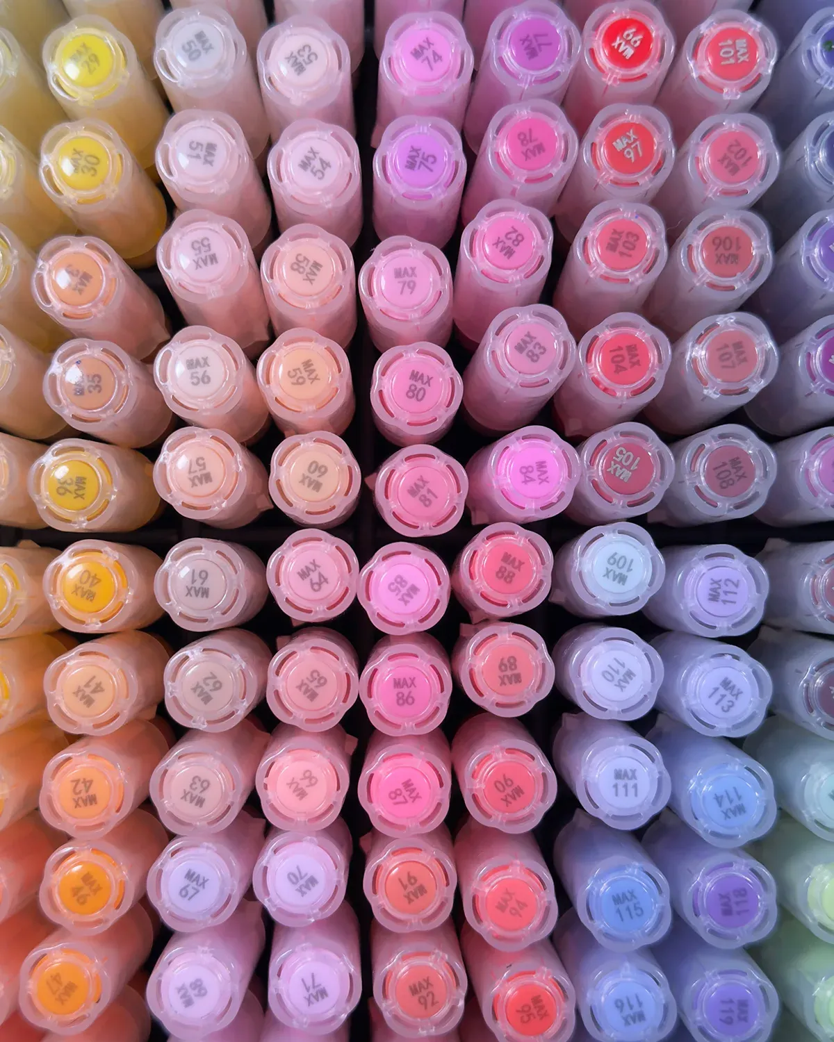 Rows of Nicety acrylic marker caps arranged by colour, from yellow and pink to purple.